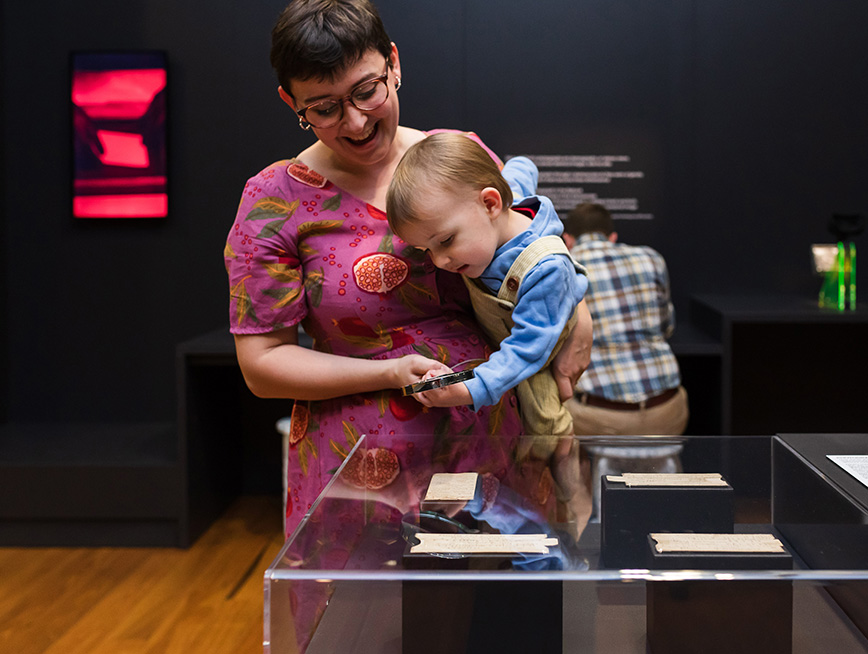 Mother carrying their baby while he looks through the exhibition glass.