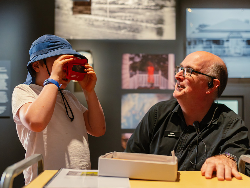 Young boy interacting with the exhibition touch trolley camera with a visitor experience officer smiling at them