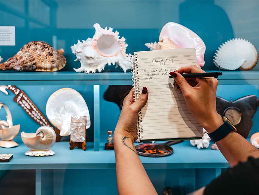 Hand writing on a notebook, against the display cabinets.
