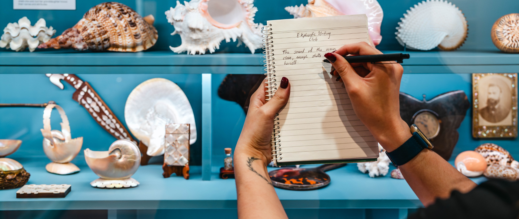 Hand writing on a notebook, against the display cabinets.