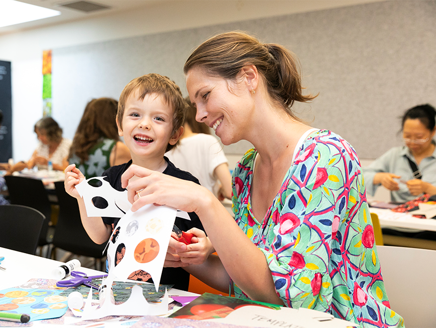 Mother and toddler son smiling as they make craft items in a studio workshop