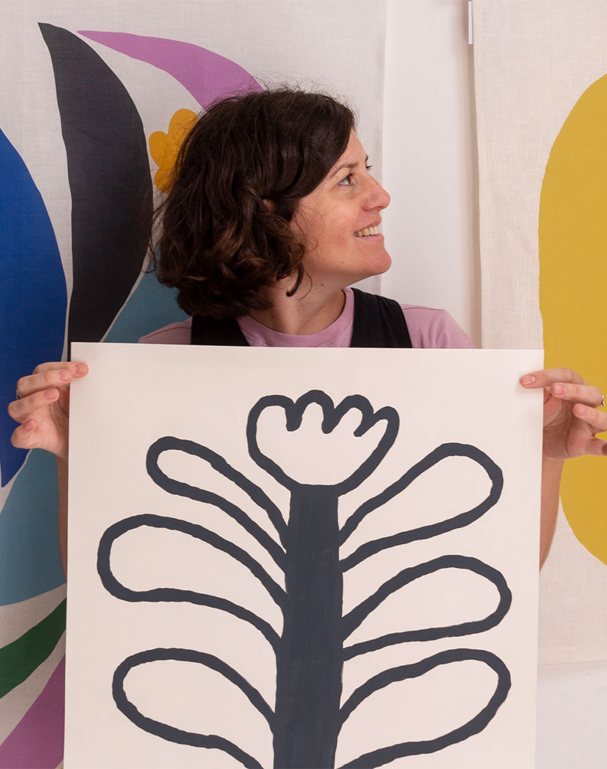 Claire Ritchie posing with her colourful artwork behind her, also holding a beautiful flower image in centre of photo