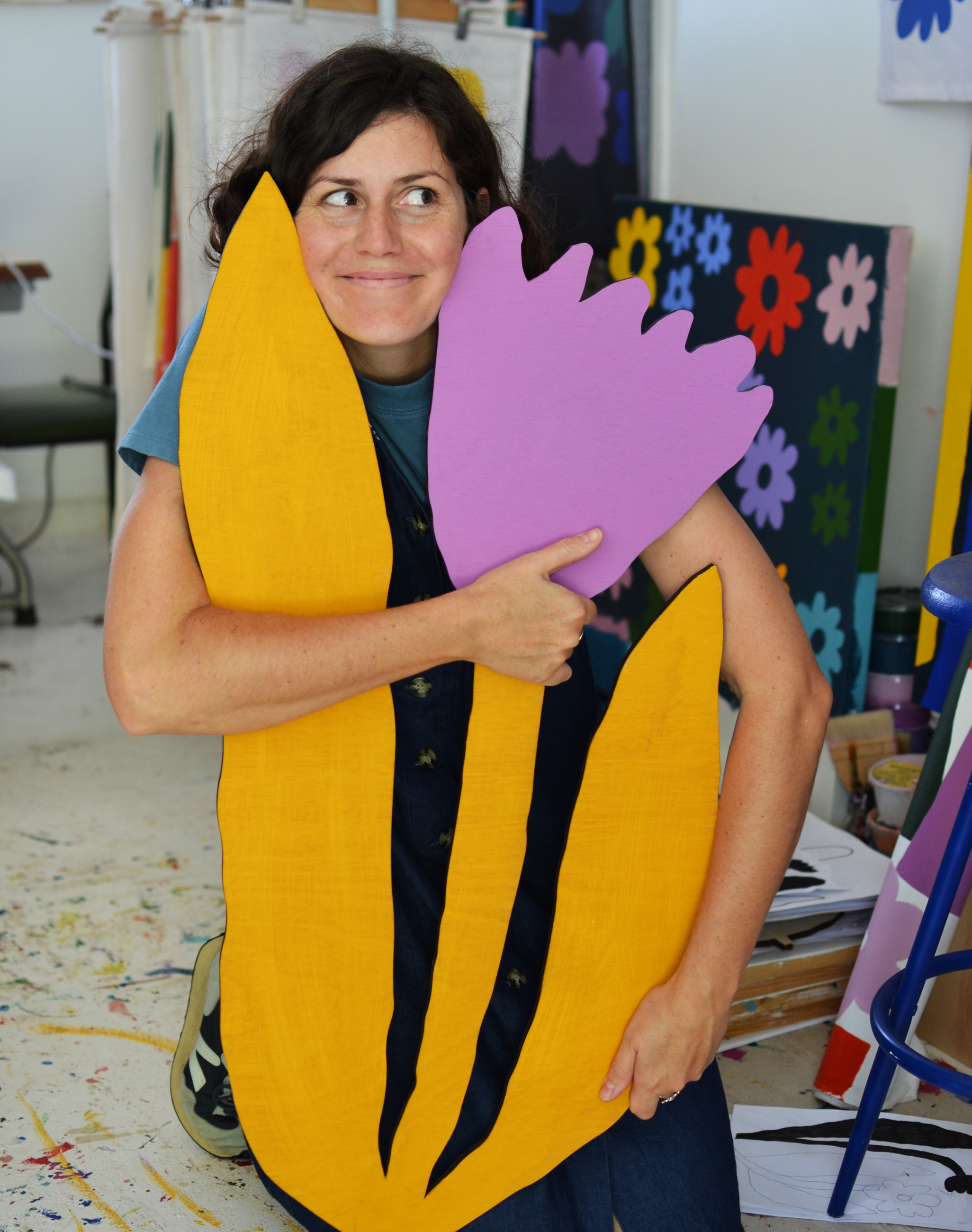 Claire Ritchie on her knees hugging a flower shaped artwork, looking happy and cheeky to the side