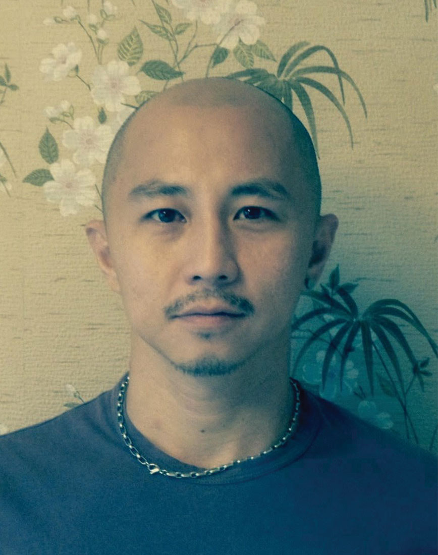 Man wearing blue shirt and silver chain staring into the camera