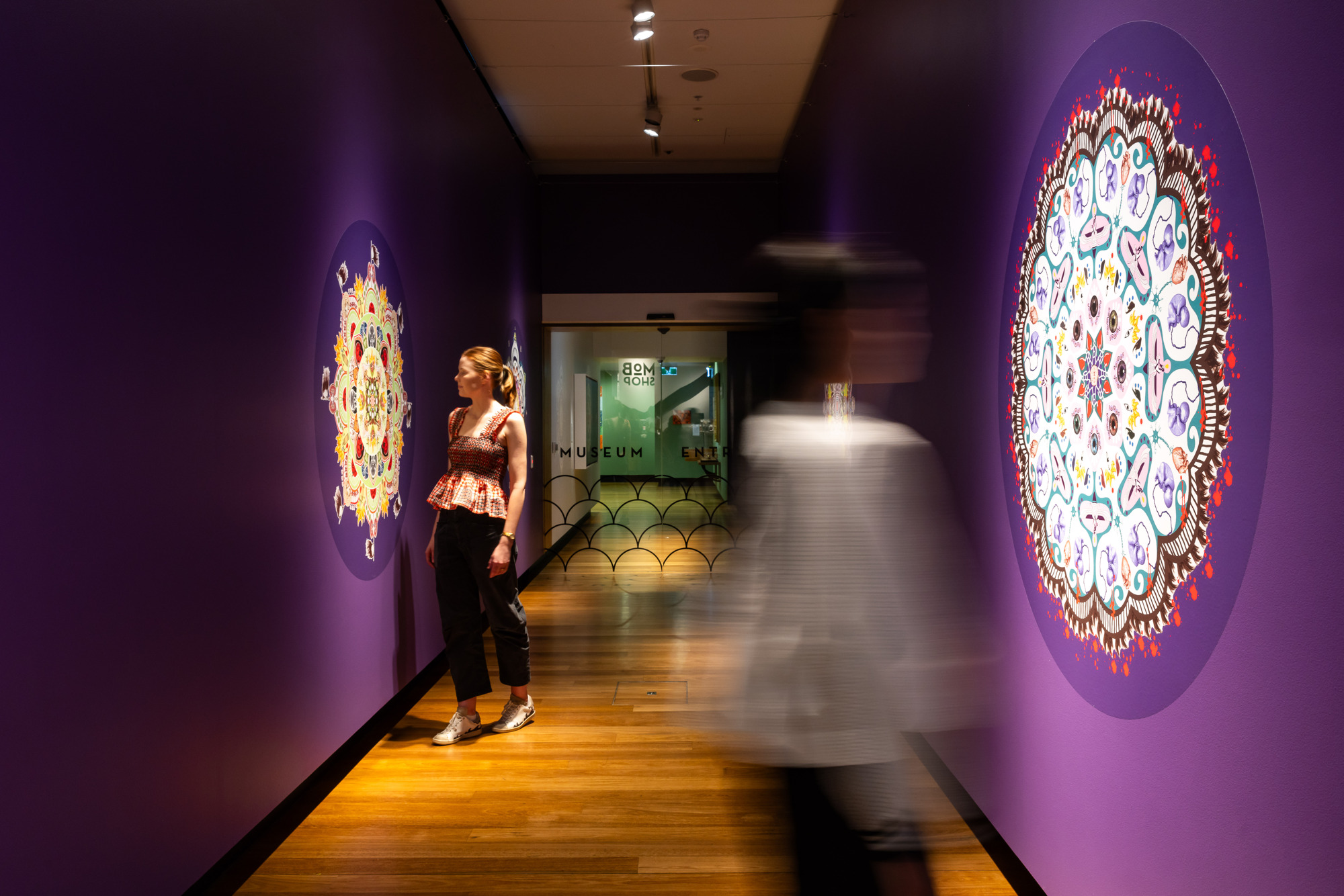 Two visitors in a purple hallway looking at art on the walls