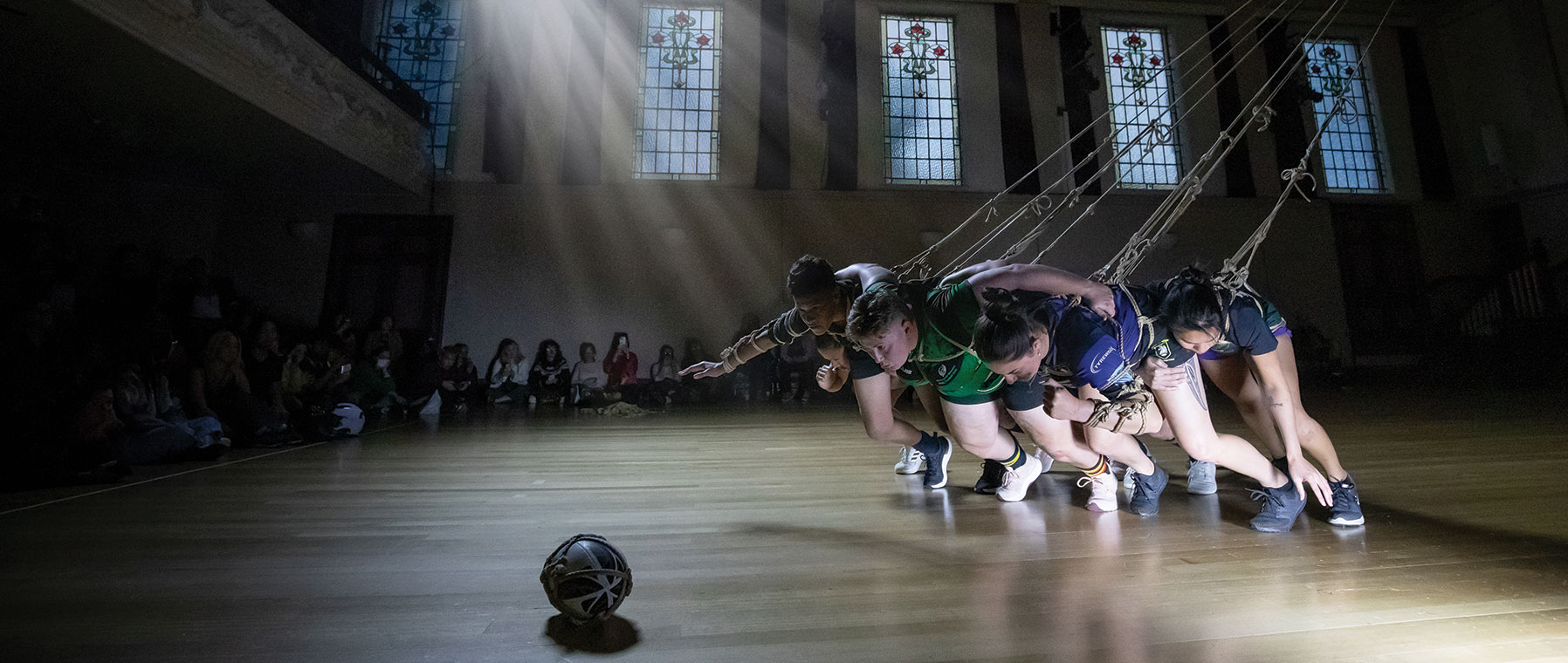 A group of people attached to ropes all pulling in the direction of a ball on the floor