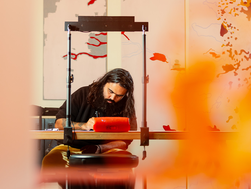 A man drawing on the table, panels of drawings are hanging behind.