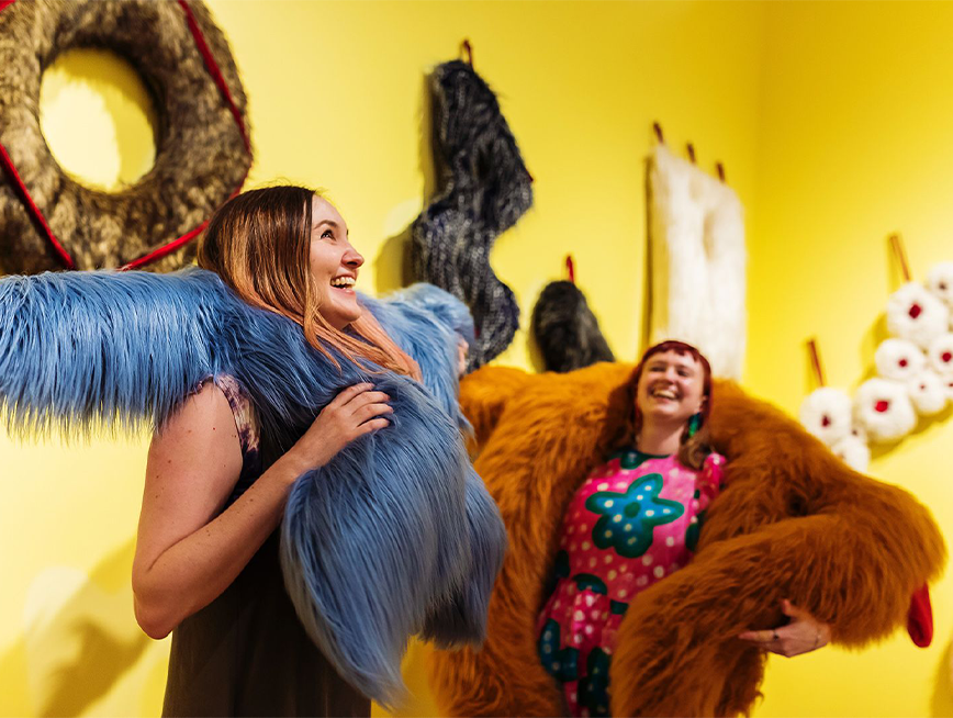 Two women inside Play Moves exhibition. One is wearing blue furry costume and another wearing brown costume.
