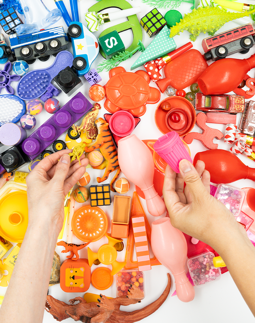 A pair of hands picking objects from a flatlay of toys.
