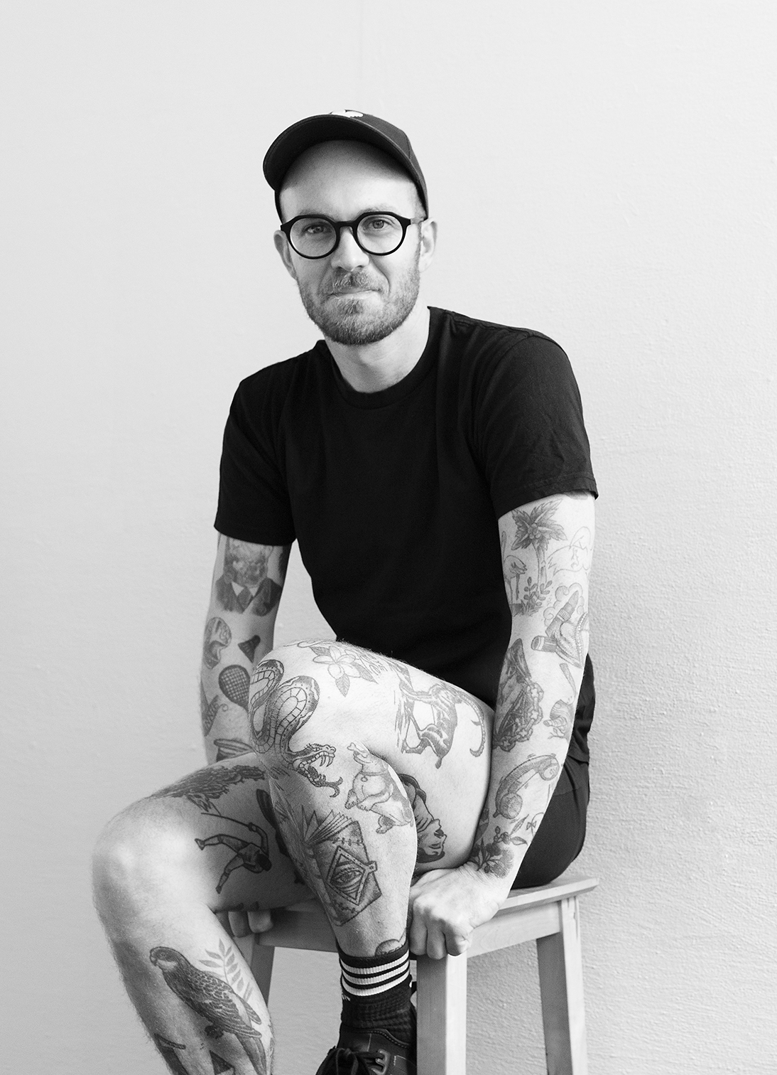 Black and white portrait of artist Gerwyn Davies sitting on a stool