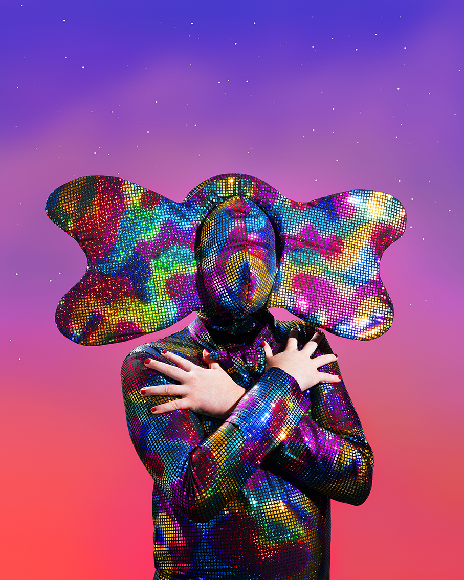 A person in a rainbow suit, hands crossed.