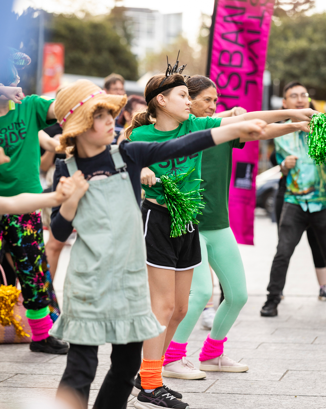 Kids wearing green clothes dancing with their hands up.