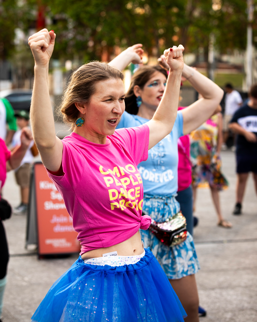 A woman in pink t-shirt and blue skirt holding their hands up.