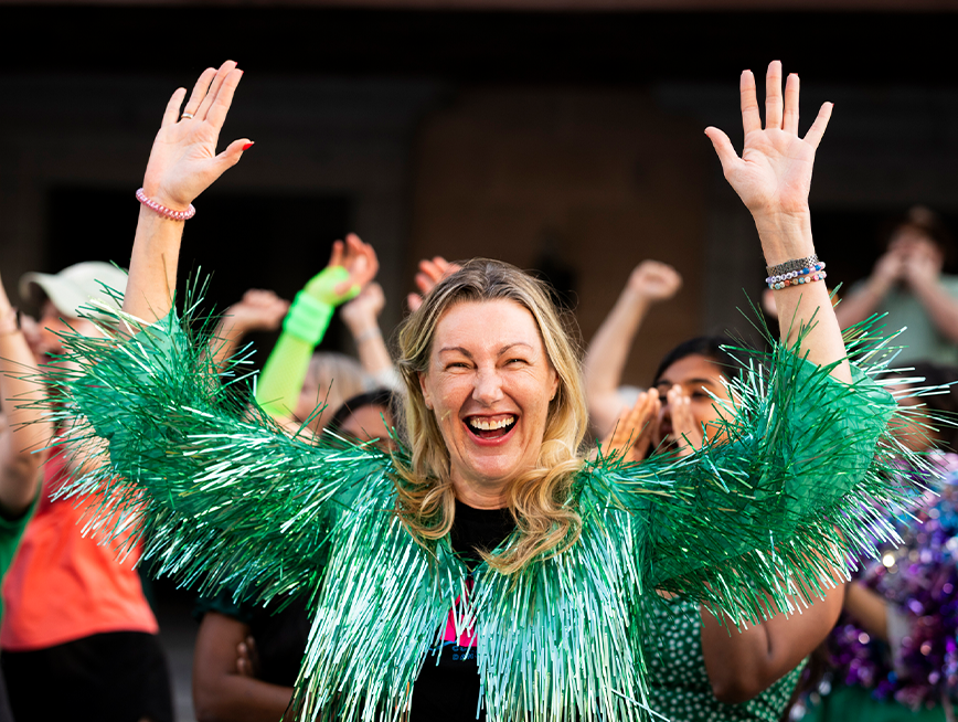 A woman in green tinsel top, smiling at the camera with her hands up.