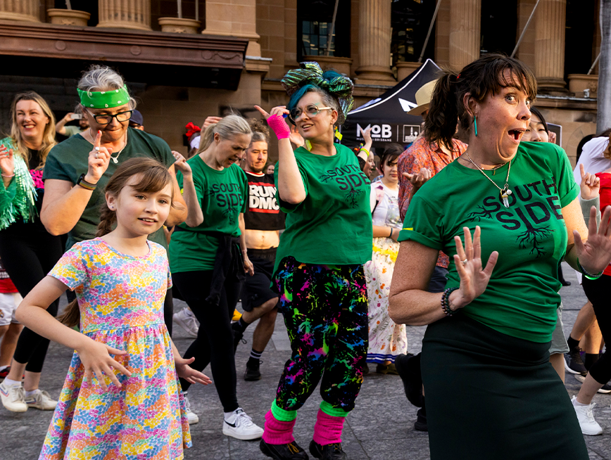 A group of people wearing green clothes, dancing and smiling at the camera.