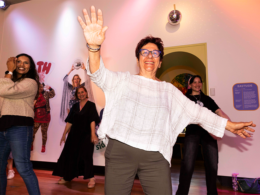 A woman dancing with her hands up, she is smiling at the camera.