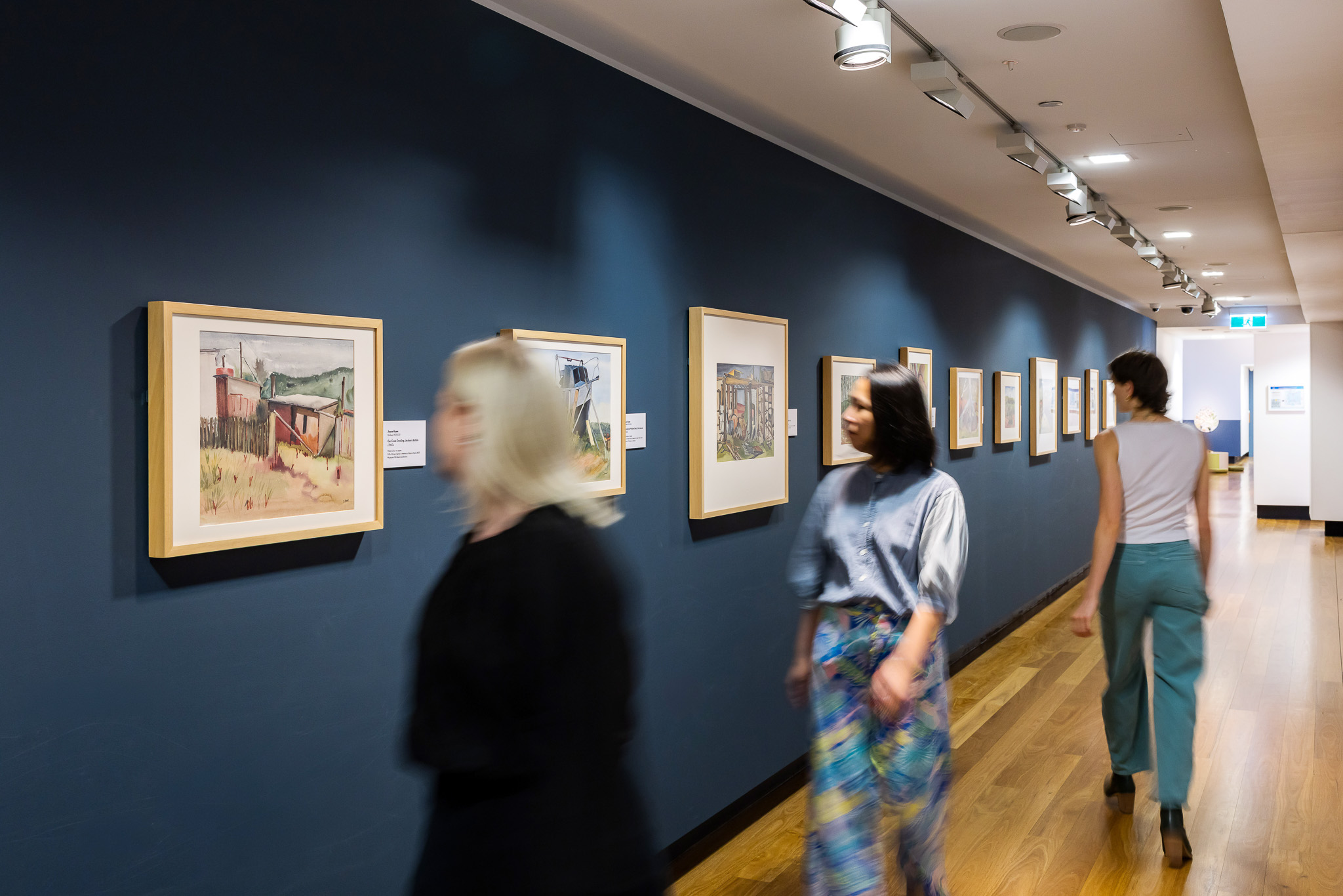 Visitors looking at a series of framed watercolour paintings by Joyce Hyam.