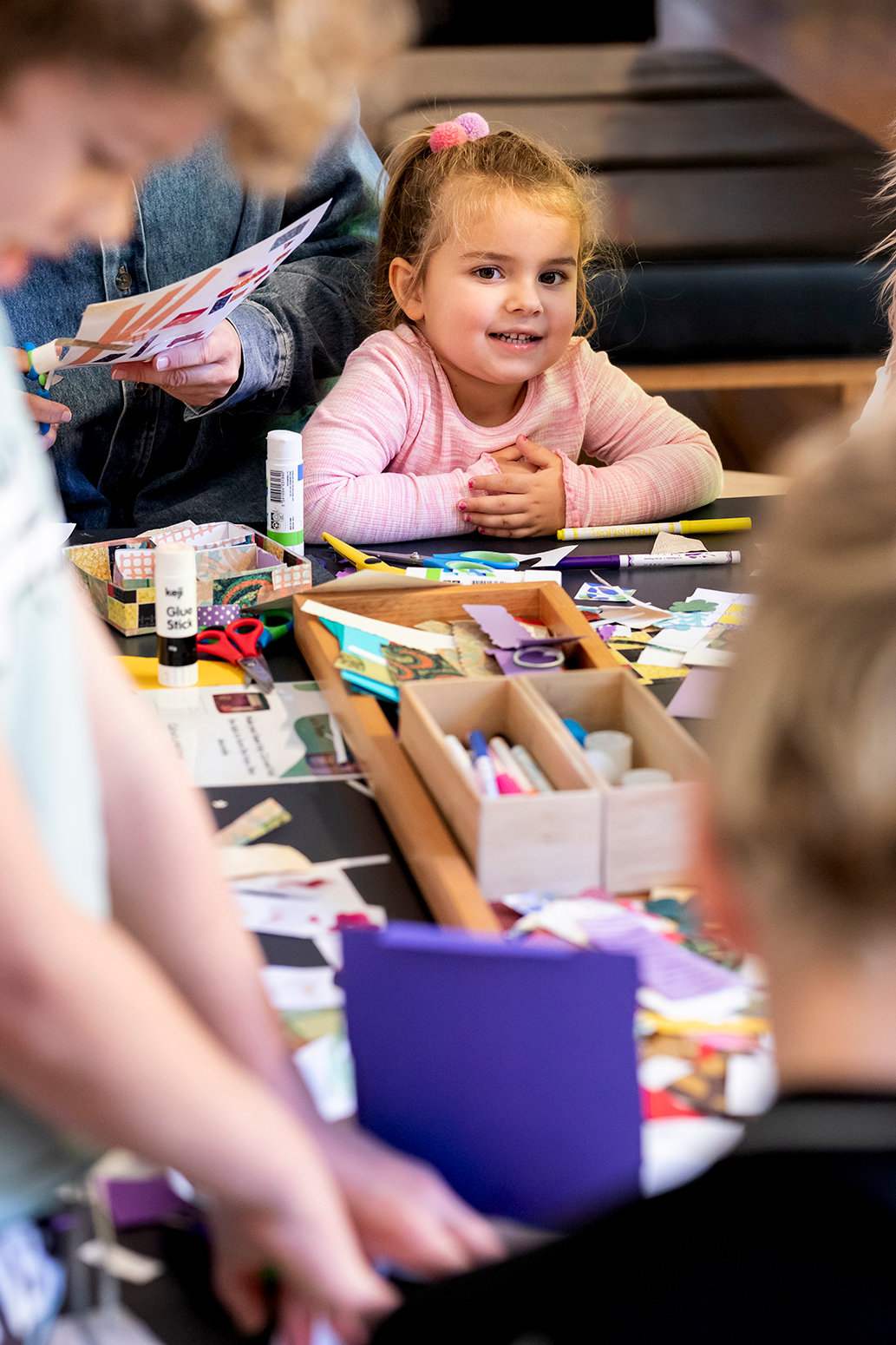 A girl sitting at the craft table, smiling at the camera.