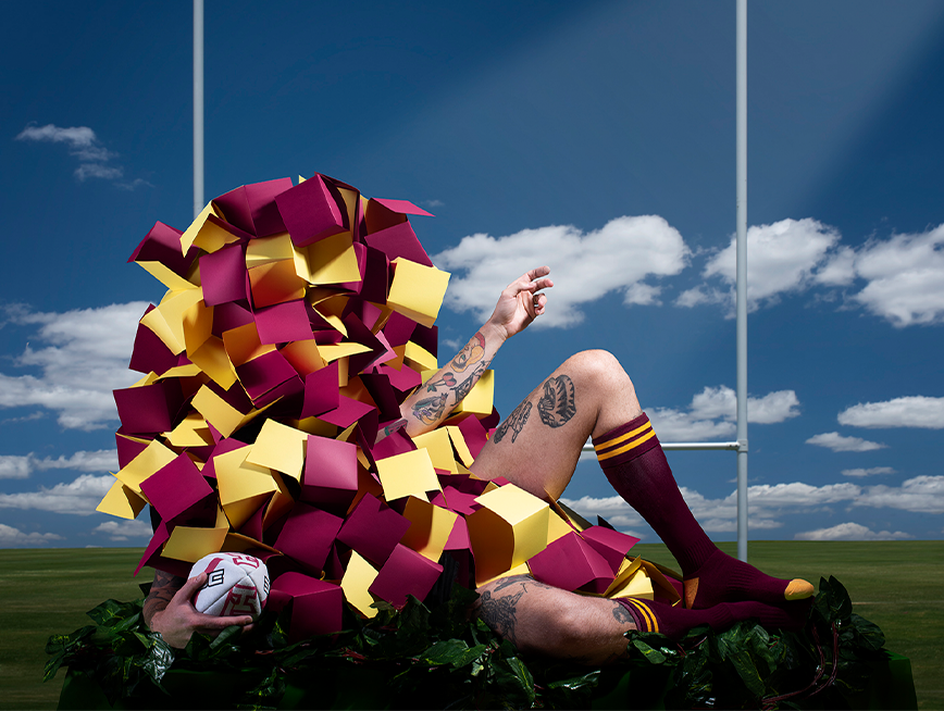 A person lies between the posts of a goal, wearing a yellow and maroon costume.