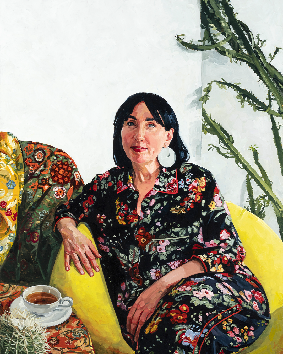 Painting of Pamela Easton seated on a bright yellow couch. A cup of tea rests beside her. She is wearing a floral top and matching pants, accessorised with large round white earrings.