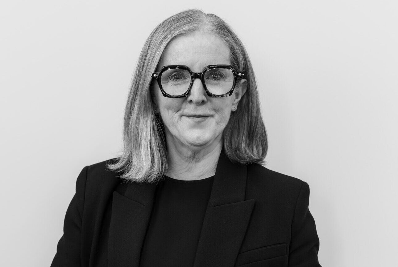Woman with shoulder length hair and wide glasses crosses her hands and looks directly into camera