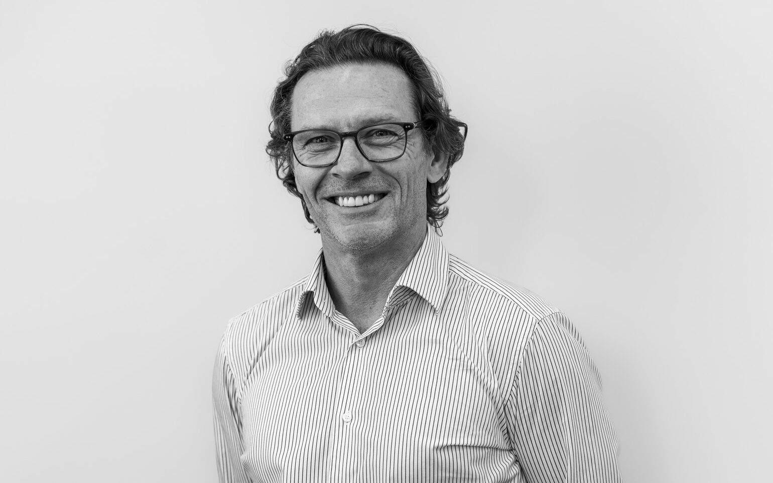 Man in a collared shirt and glasses smiles at camera