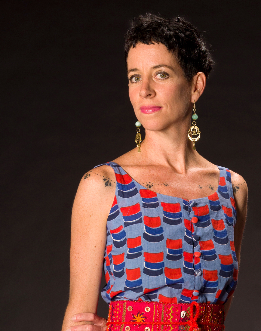 The artist Kirstie Macleod wearing a patterned top and embroyered belt, looking at the camera.