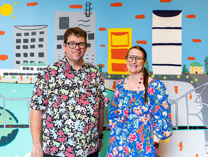 Martin and Pia standing in front of his mural, smiling in front of the camera.