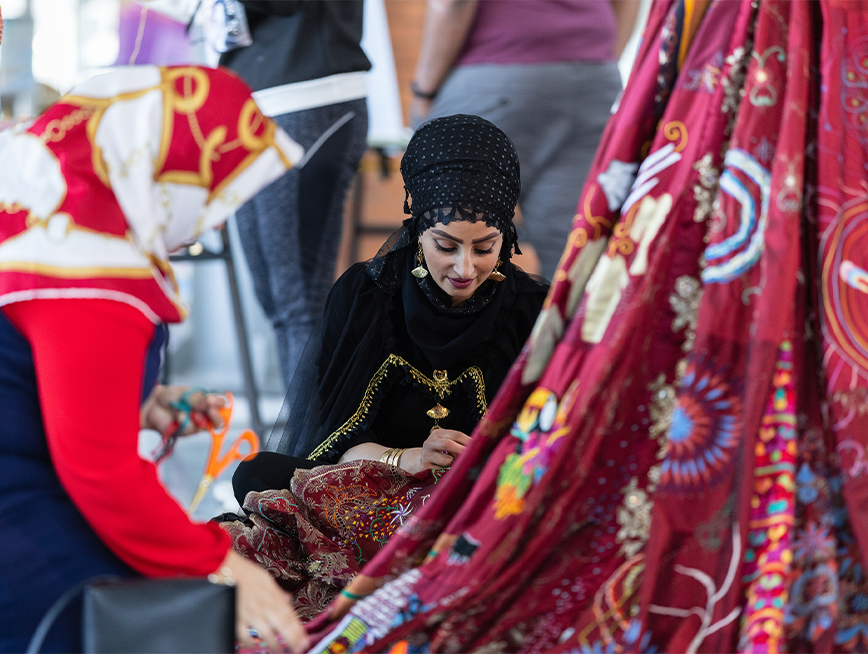 Two embroiderers working on the red dress.