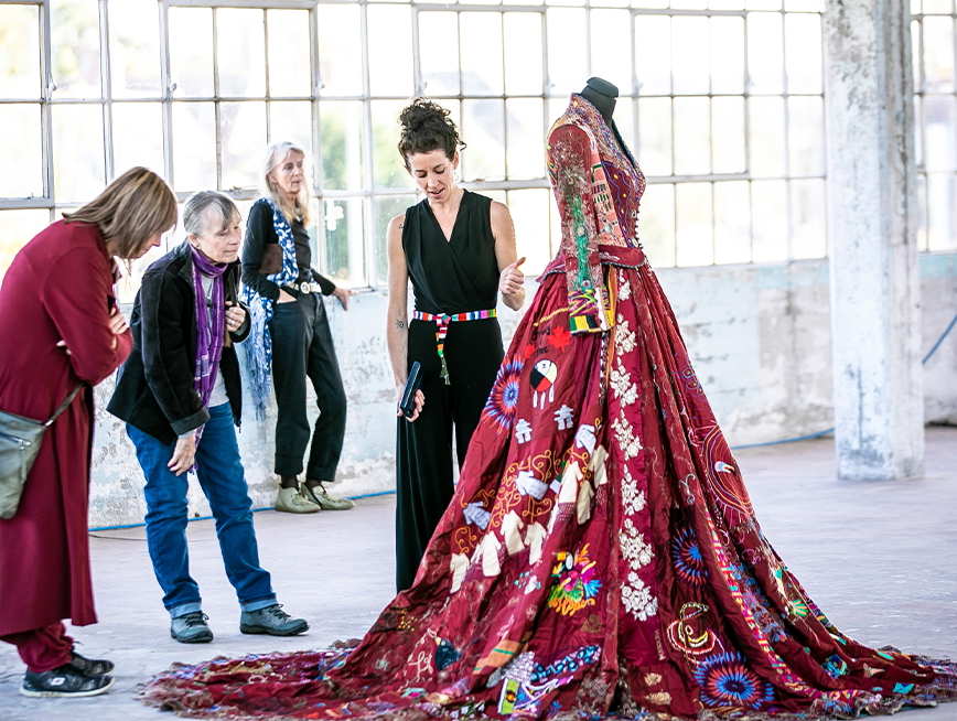 The artist Kirstie and audience looking at a embroidered red dress.