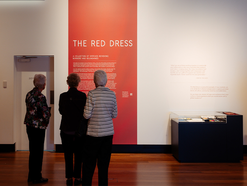 Three visitors reading The Red Dress didactics on the wall.