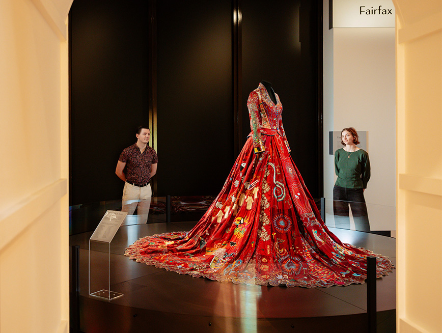 In the gallery, two visitors looking at a delicately embroidered red dress.