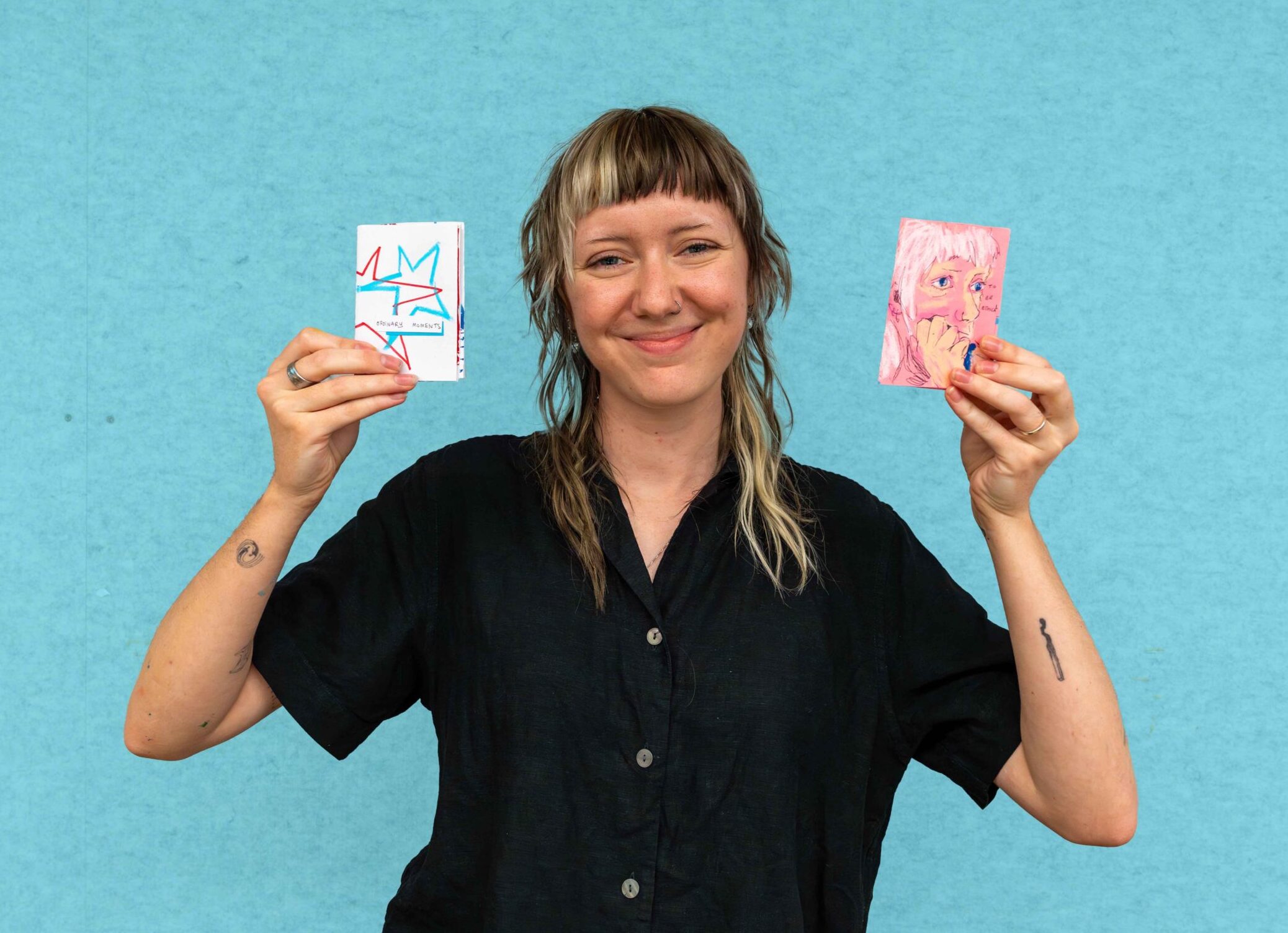 Young woman smiling and holding uo two zines in both hands