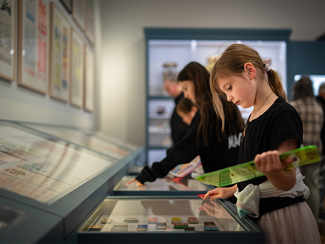 A girl is holding a clipboard looking at objects inside the blue drawer.