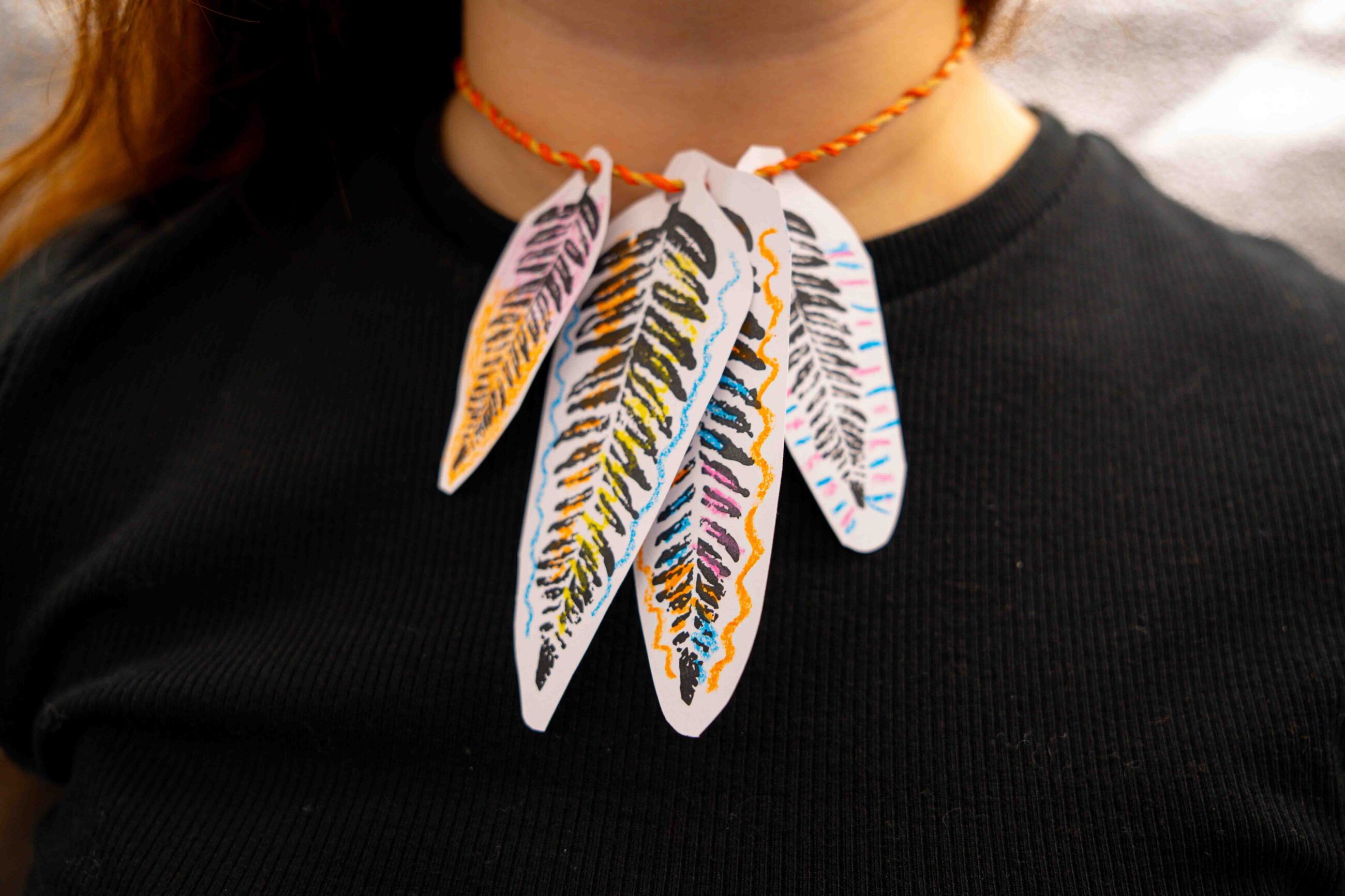 Woman wearing a necklace made from raffia and paper fern cut-outs.