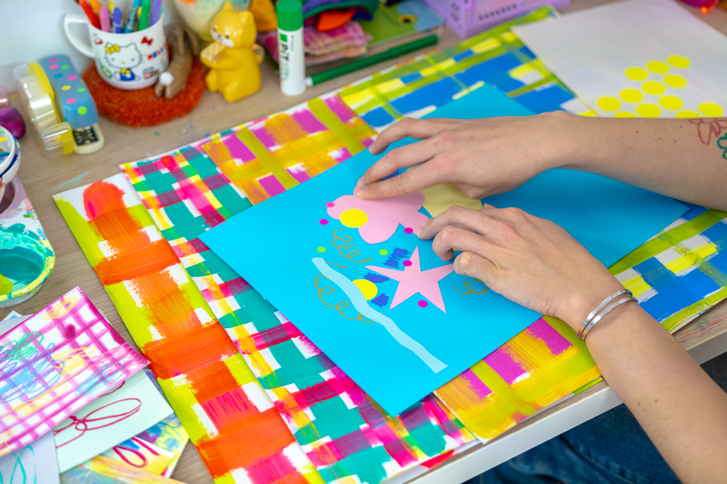 A pair of hands collaging with colour paper on the workshop table.