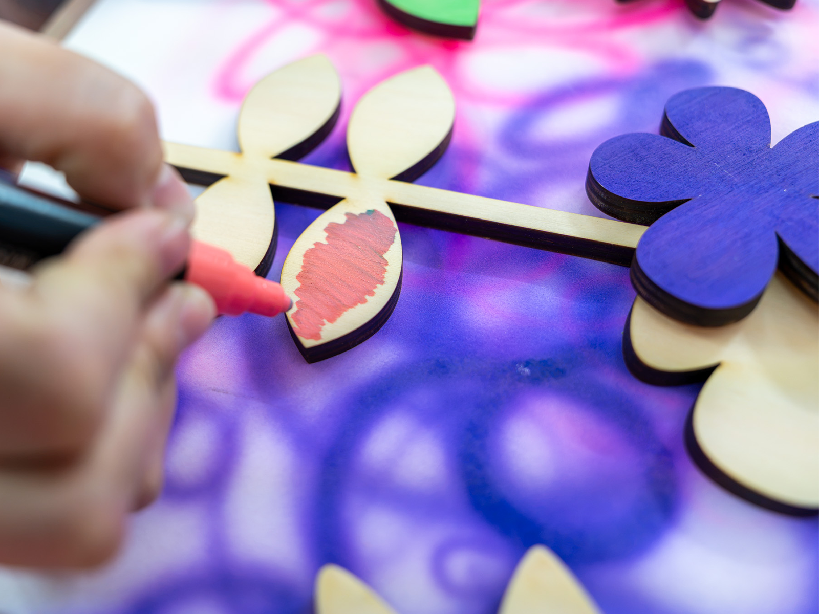 A hand painting wooden flowers in pink and purple.