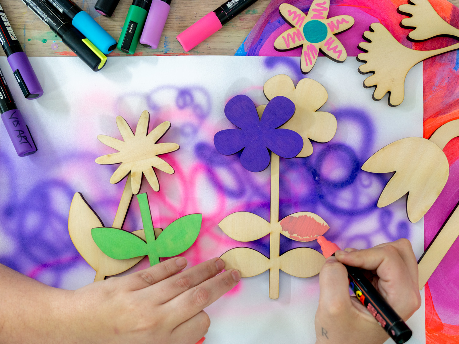 Hands painting wooden flowers in pink, green and purple.