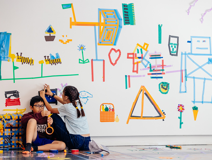 Two kids are surrounded by colourful tapes in the gallery.