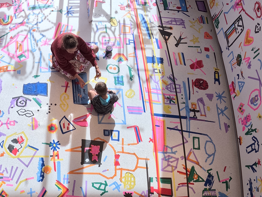 Mum and son sitting at a gallery full of colourful tapes.