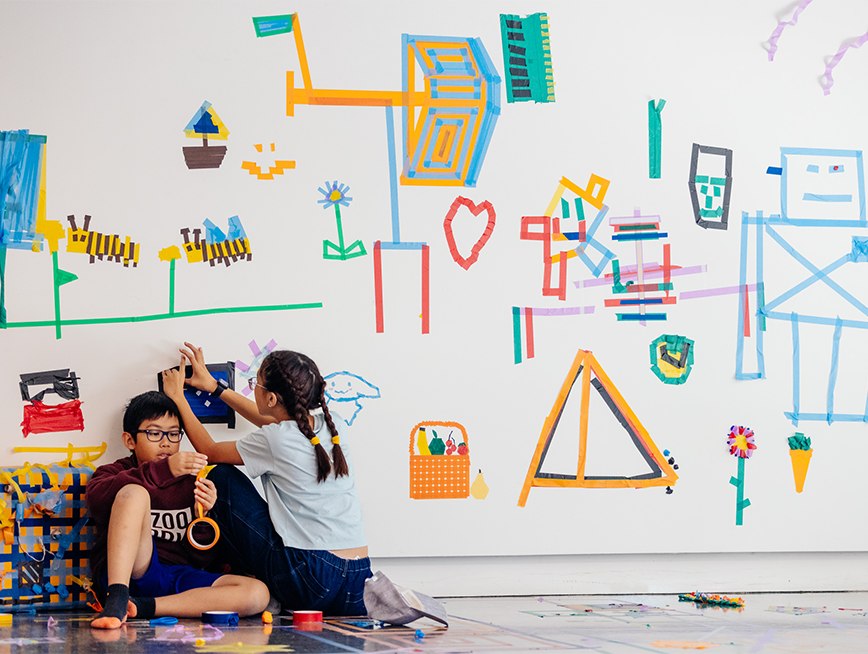 A boy and a girl making tape drawings on the gallery wall.